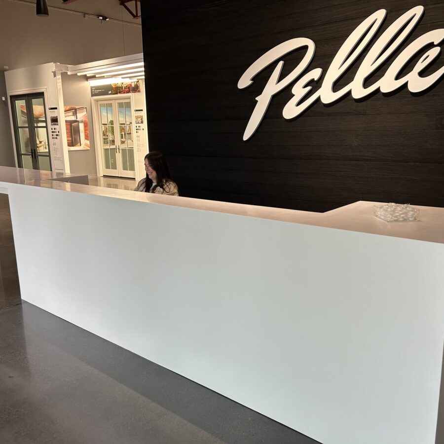 Reception area with a white counter, a person seated behind it, and “Pelle” displayed in large letters on a dark wall.